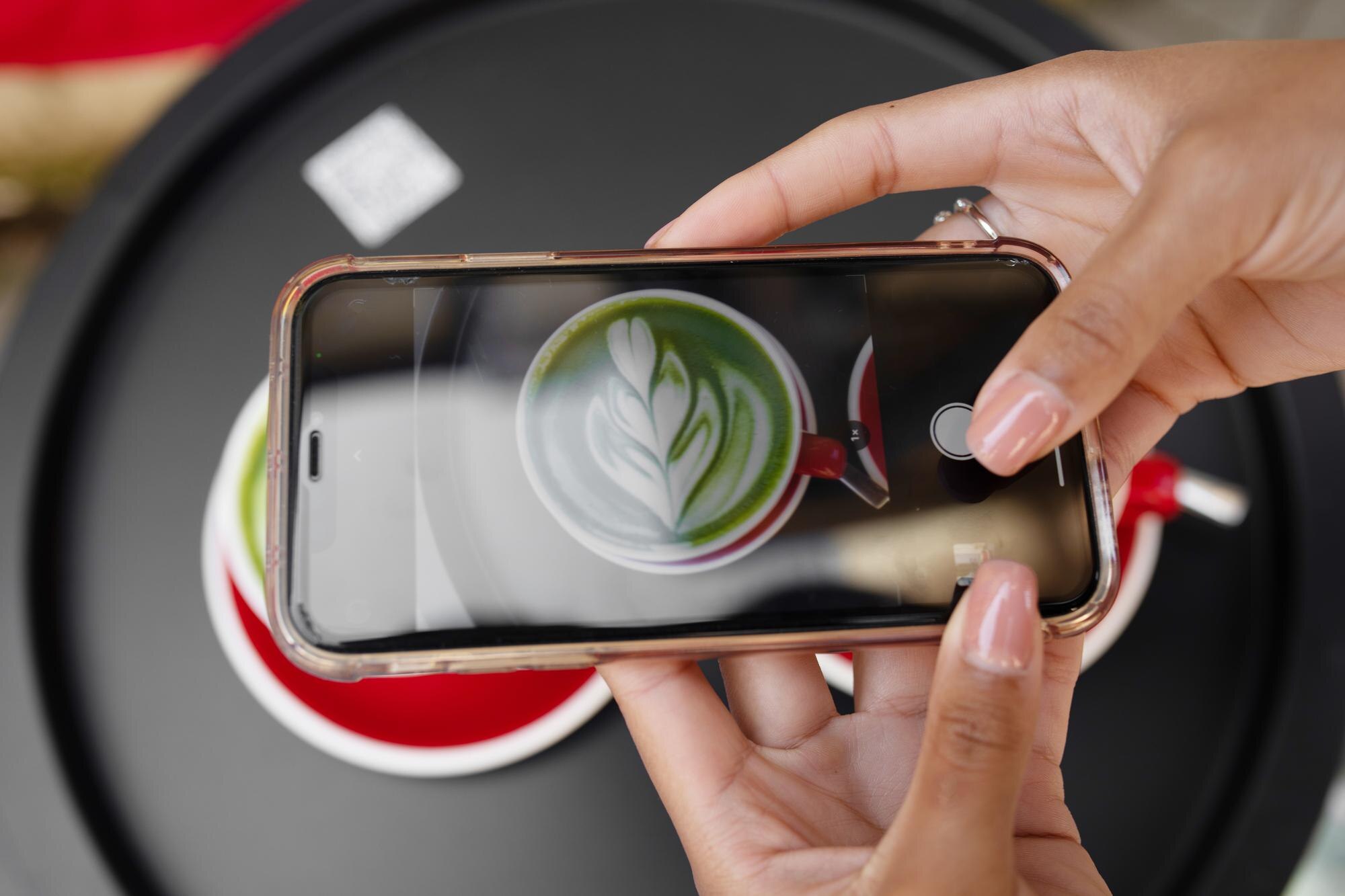 Młoda dziewczyna używa fotografii smartfona z kawą latte art na mobilnym aparacie