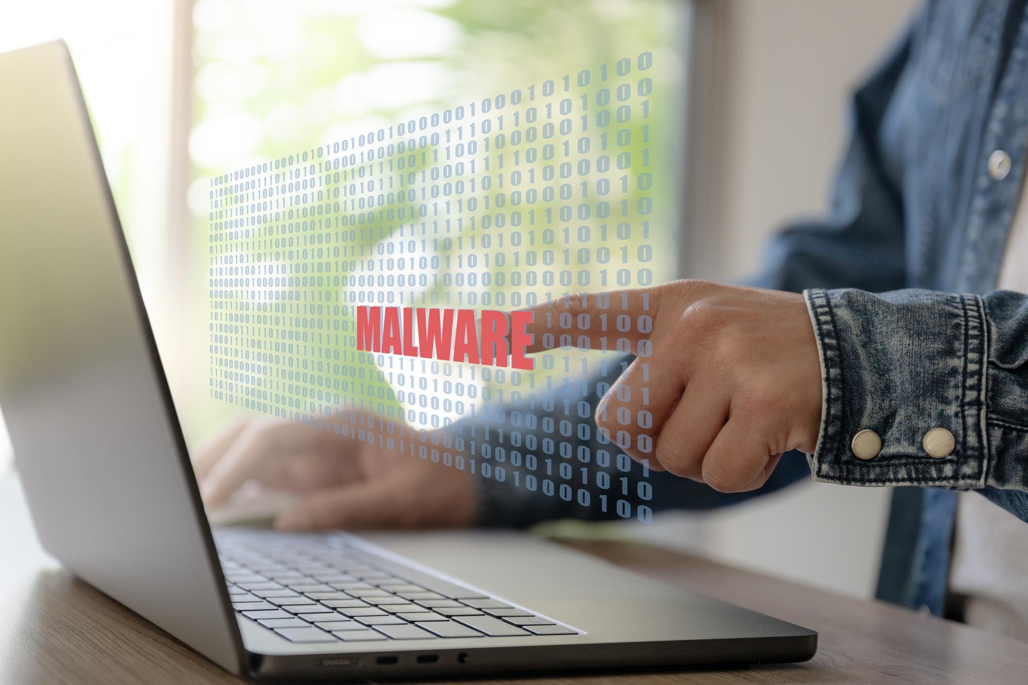 Biznesmen pracuje z laptopem i ręcznie uderza w tekst Malware